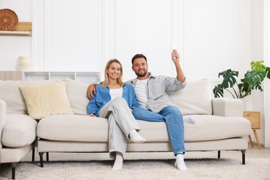 Photo of Couple using remote to control air conditioner on sofa at home