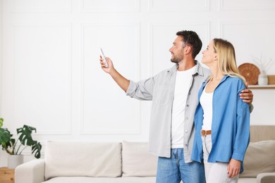 Photo of Couple using remote to control air conditioner at home. Space for text