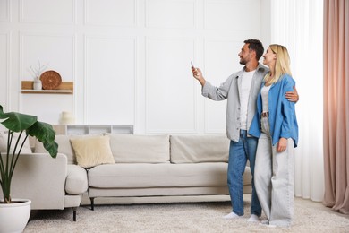 Photo of Couple using remote to control air conditioner at home. Space for text
