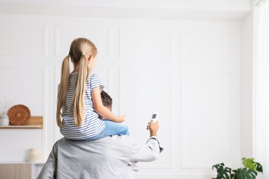 Photo of Father and daughter using remote to control air conditioner at home, back view. Space for text