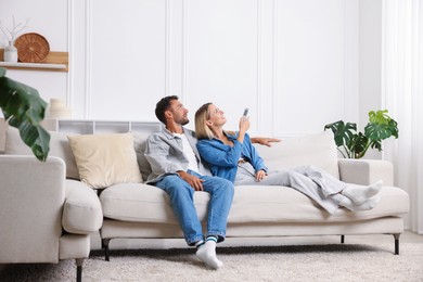 Photo of Couple using remote to control air conditioner on sofa at home