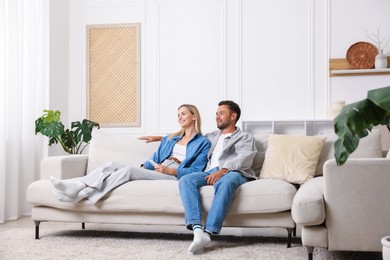 Photo of Couple with air conditioner remote control on sofa at home