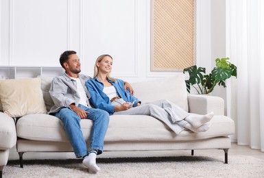 Photo of Couple with air conditioner remote control on sofa at home