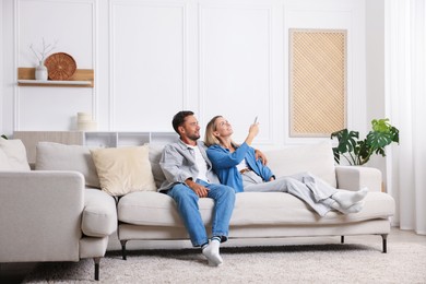 Photo of Couple using remote to control air conditioner on sofa at home