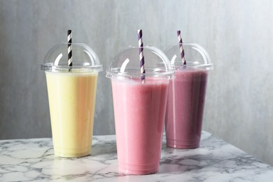 Photo of Milkshakes of different flavors in plastic cups on white marble table, closeup