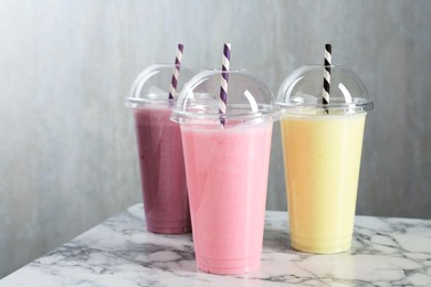 Photo of Milkshakes of different flavors in plastic cups on white marble table, closeup