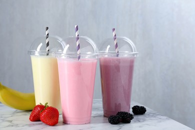Photo of Milkshakes of different flavors in plastic cups and ingredients on white marble table, closeup