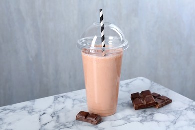 Photo of Tasty milkshake in plastic cup and chocolate pieces on white marble table