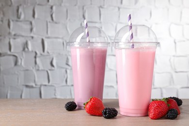 Photo of Tasty milkshakes in plastic cups and fresh berries on wooden table, closeup