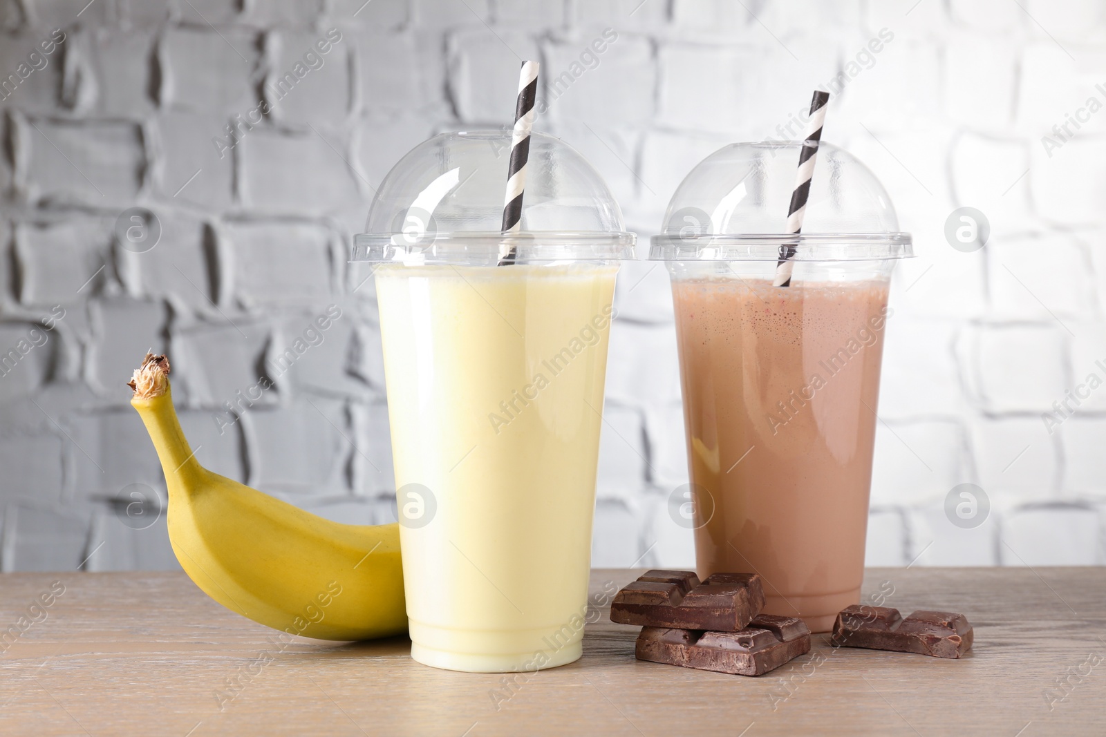 Photo of Tasty milkshakes in plastic cups and ingredients on wooden table, closeup