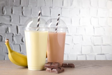 Photo of Tasty milkshakes in plastic cups and ingredients on wooden table, closeup. Space for text