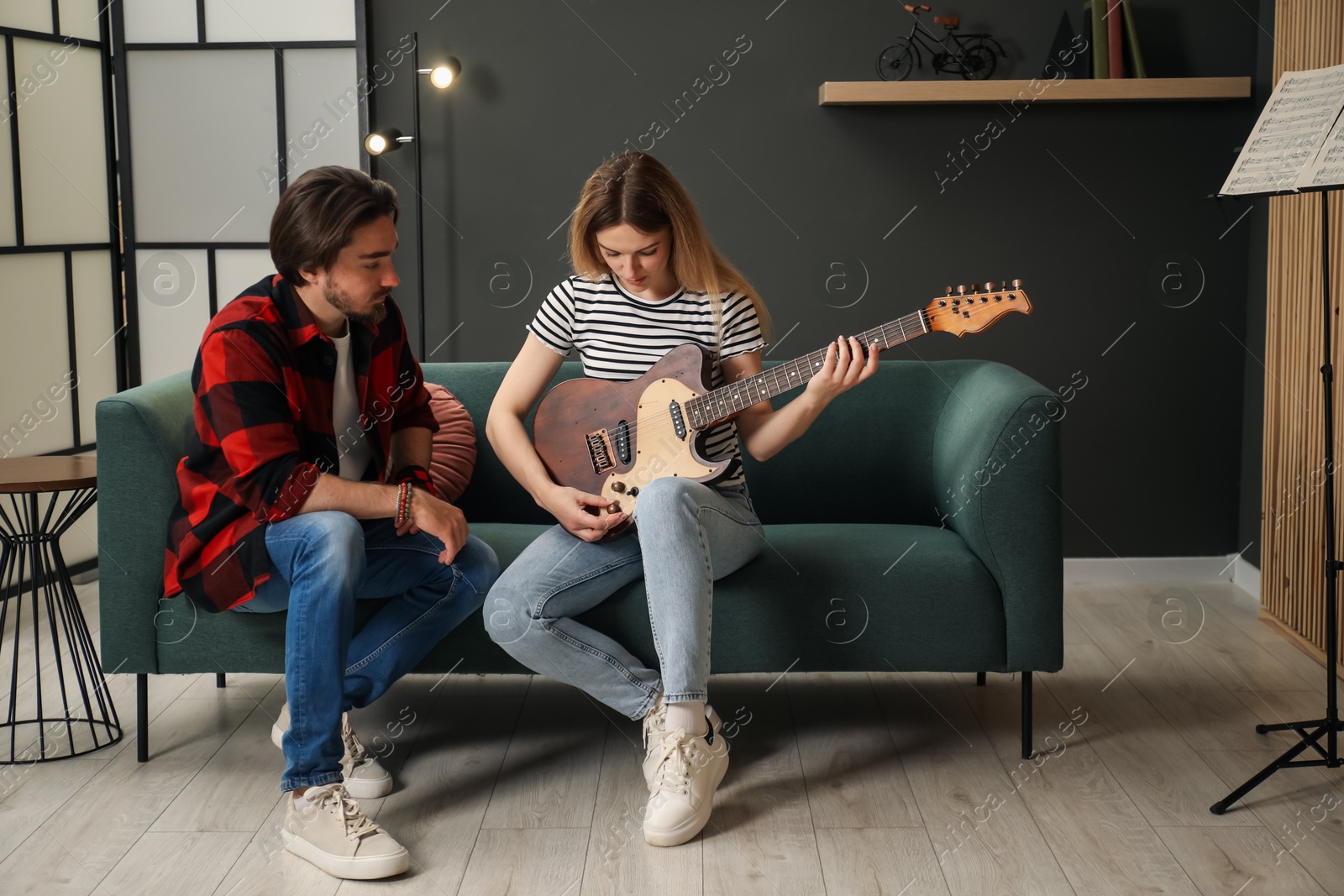 Photo of Tutor teaching woman to play guitar on sofa at home