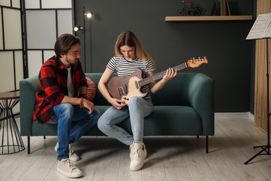 Photo of Tutor teaching woman to play guitar on sofa at home