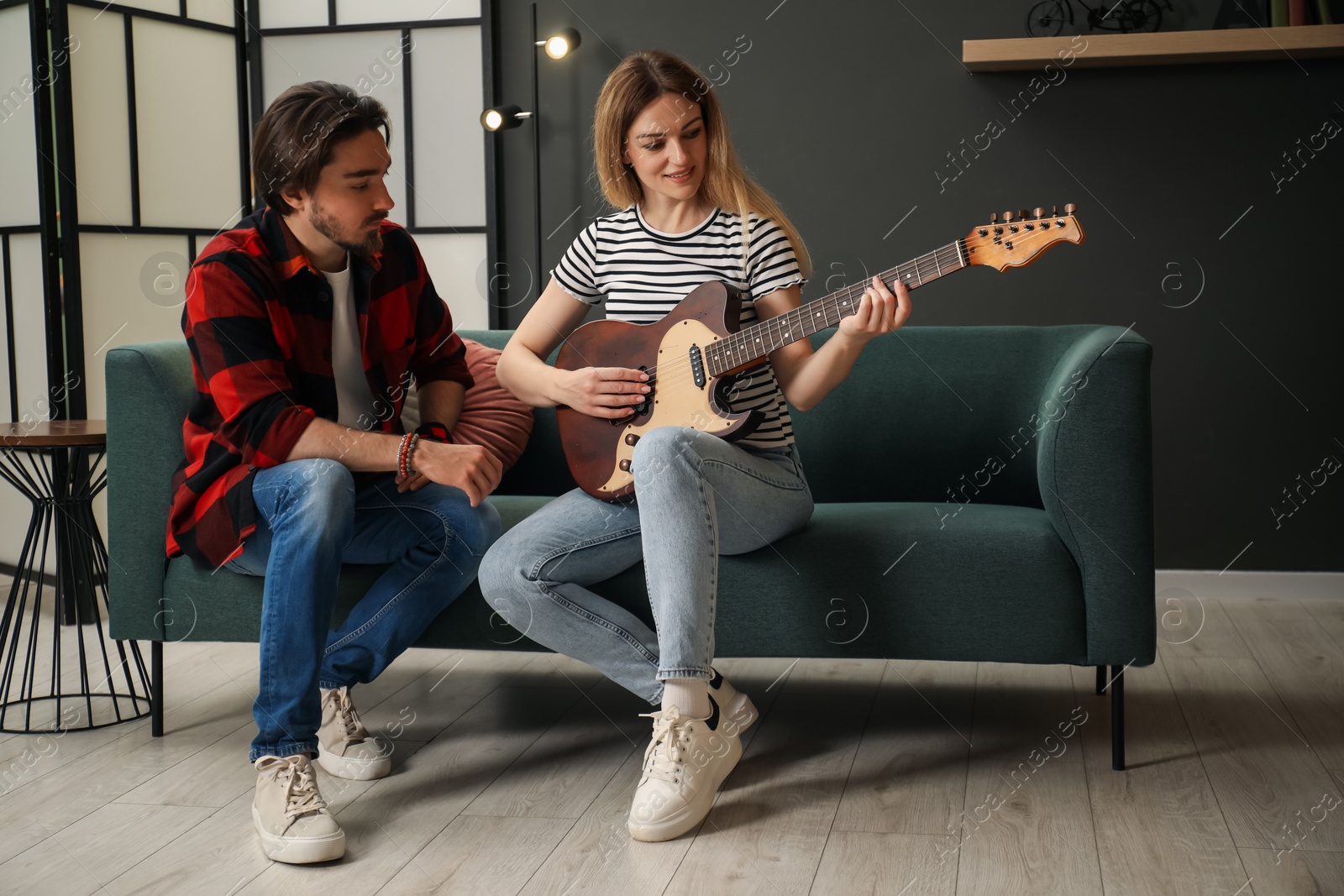 Photo of Tutor teaching woman to play guitar on sofa at home