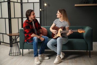 Photo of Tutor teaching woman to play guitar on sofa at home