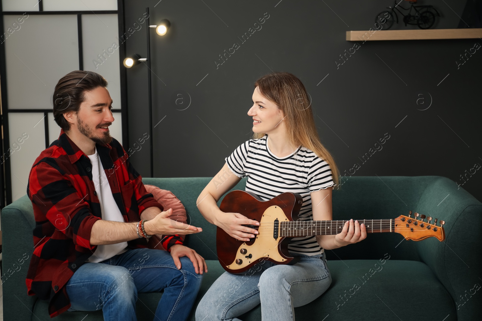 Photo of Tutor teaching woman to play guitar on sofa at home