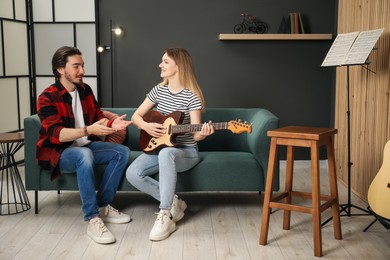 Photo of Tutor teaching woman to play guitar on sofa at home