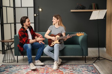 Photo of Tutor teaching woman to play guitar on sofa at home