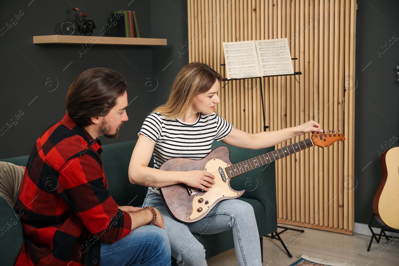 Photo of Tutor teaching woman to play guitar on sofa at home