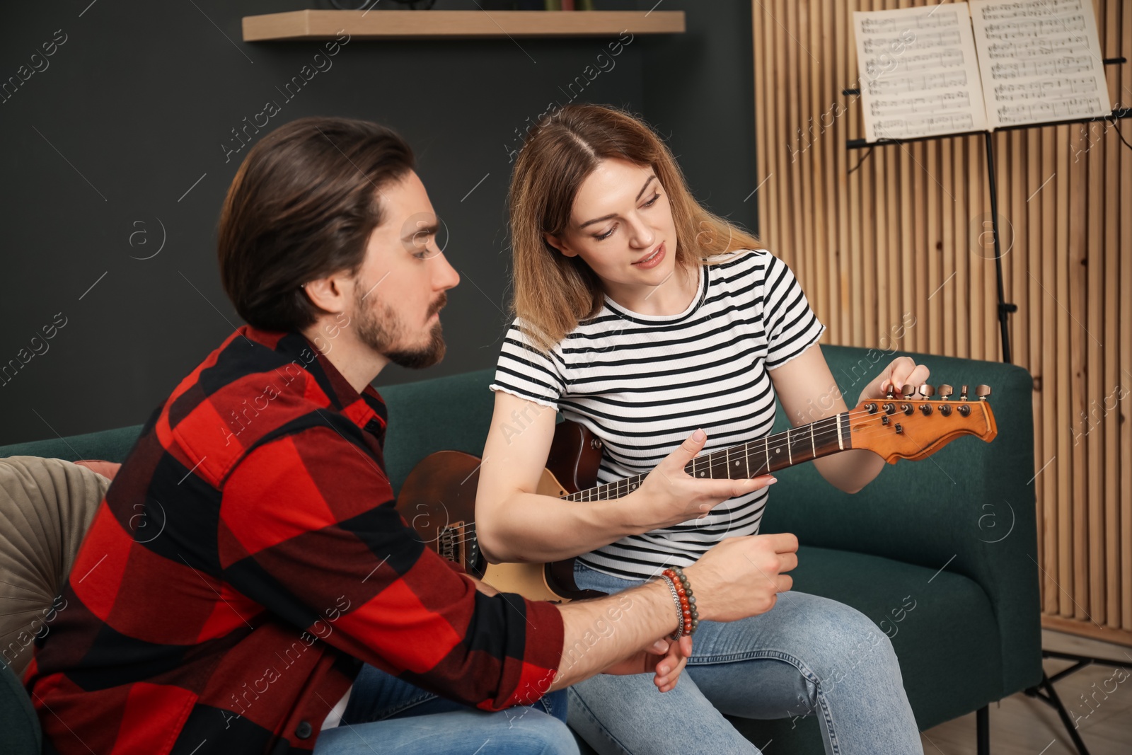Photo of Tutor teaching woman to play guitar on sofa at home