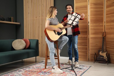 Photo of Tutor teaching woman to play guitar indoors
