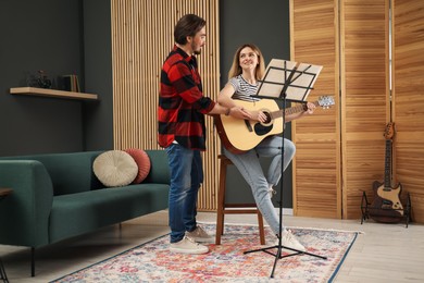 Photo of Tutor teaching woman to play guitar indoors