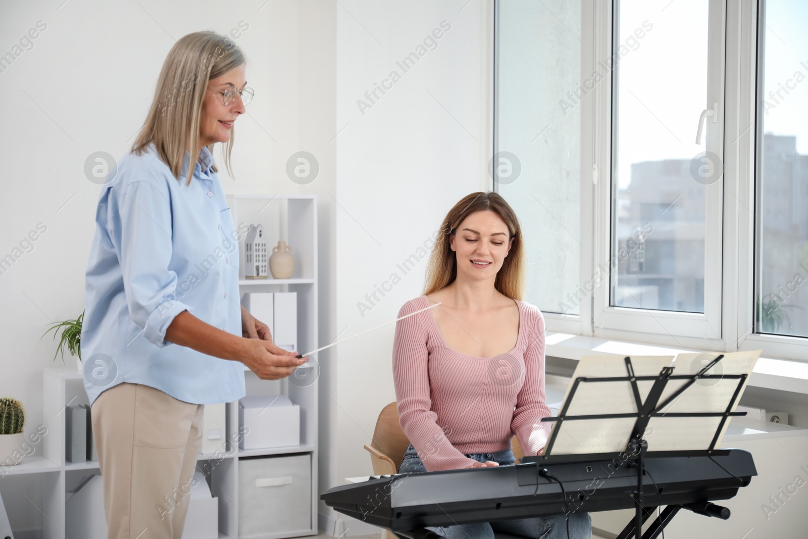 Photo of Tutor teaching woman to play piano indoors