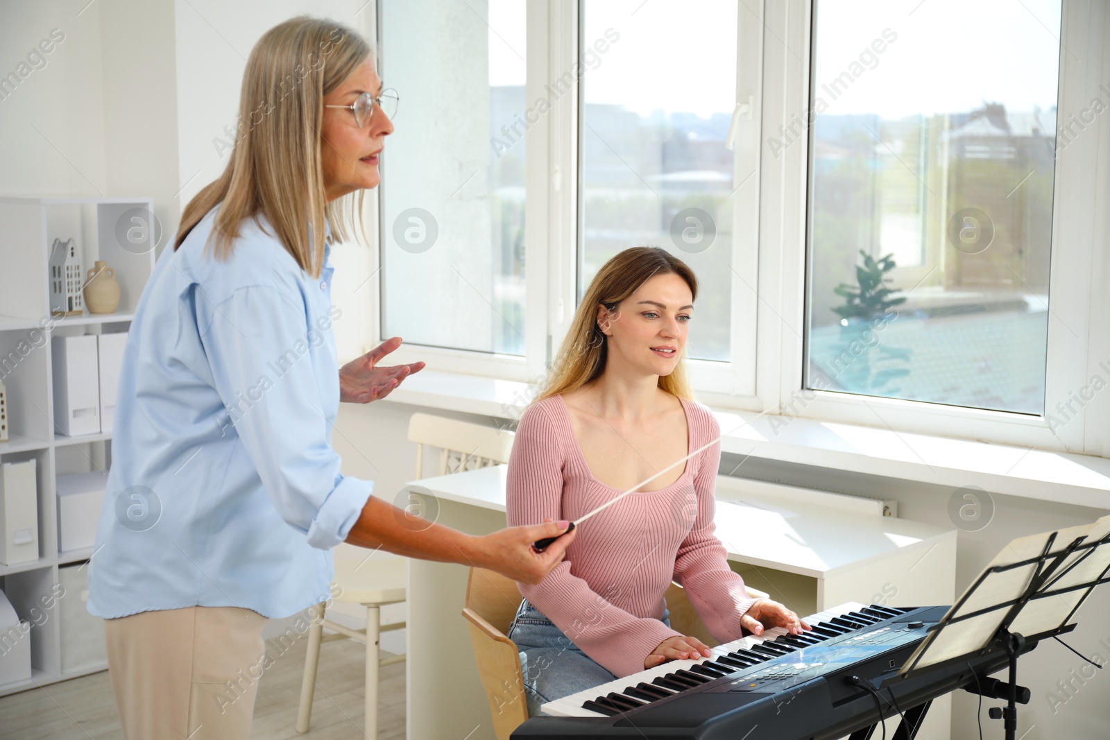 Photo of Tutor teaching woman to play piano indoors