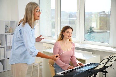Photo of Tutor teaching woman to play piano indoors