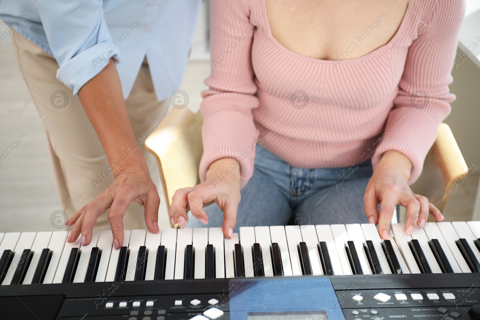 Photo of Tutor teaching woman to play piano indoors, closeup
