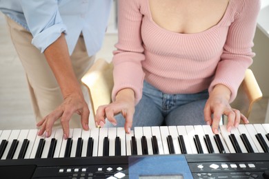 Photo of Tutor teaching woman to play piano indoors, closeup