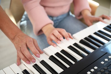 Photo of Tutor teaching woman to play piano indoors, closeup
