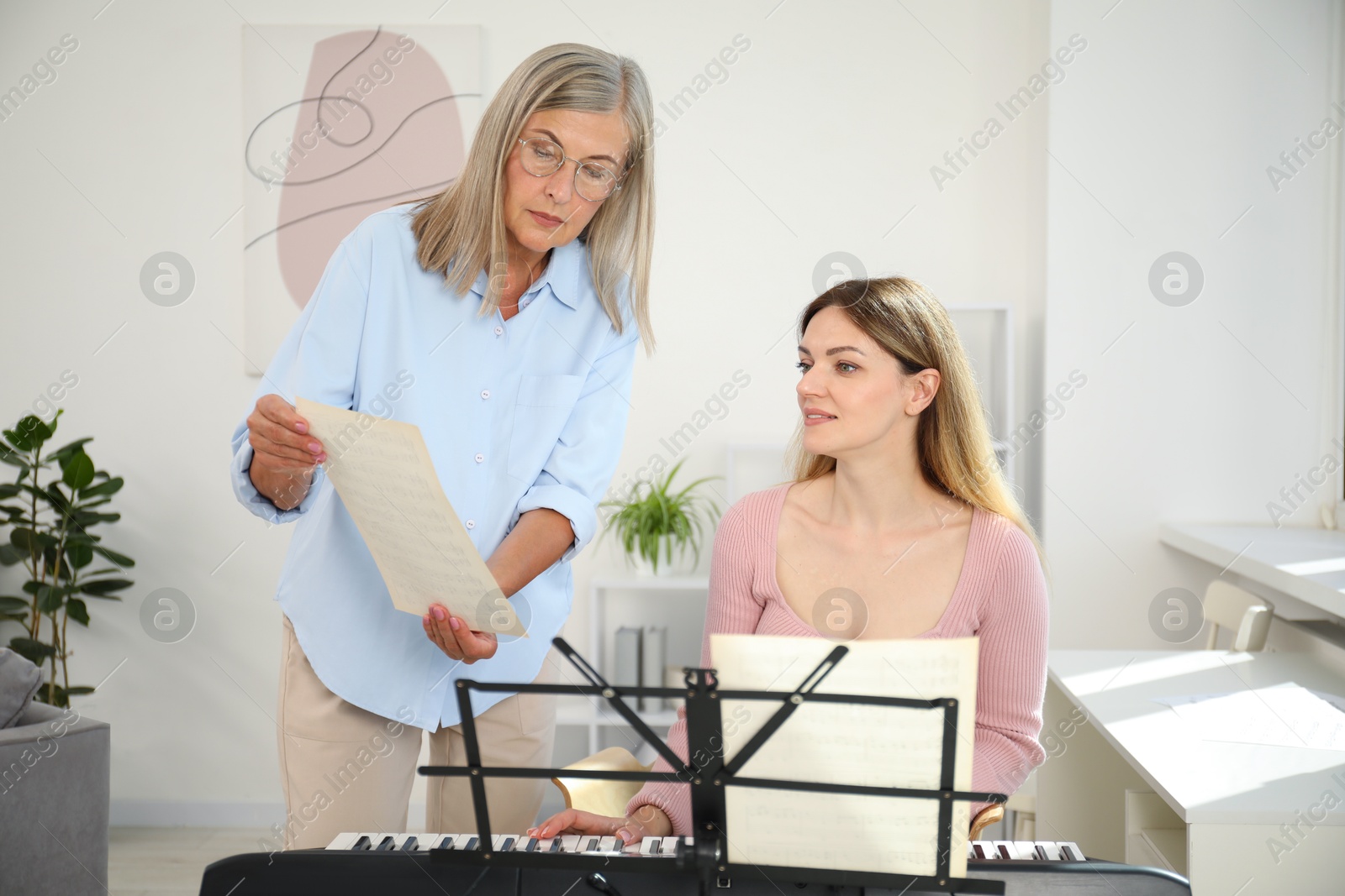 Photo of Tutor teaching woman to play piano indoors