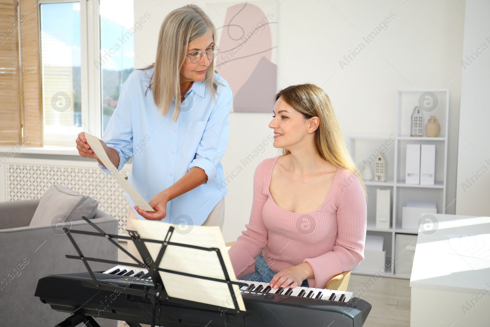 Photo of Tutor teaching woman to play piano indoors