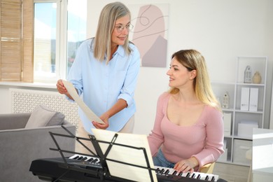 Photo of Tutor teaching woman to play piano indoors