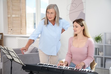 Photo of Tutor teaching woman to play piano indoors