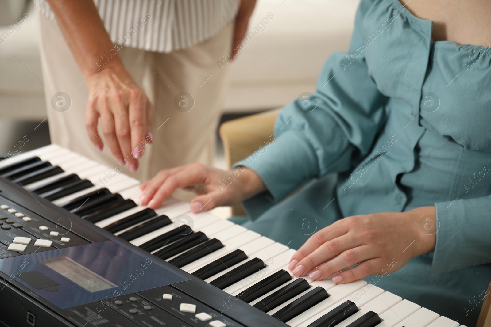 Photo of Tutor teaching woman to play piano indoors, closeup