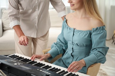 Photo of Tutor teaching woman to play piano indoors, closeup