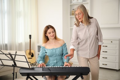 Photo of Tutor teaching woman to play piano indoors