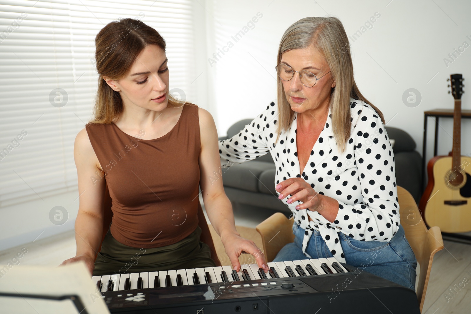 Photo of Tutor teaching woman to play piano indoors