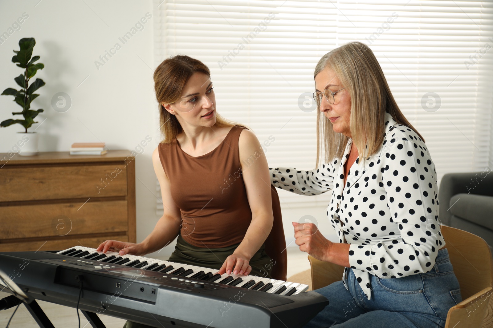 Photo of Tutor teaching woman to play piano indoors
