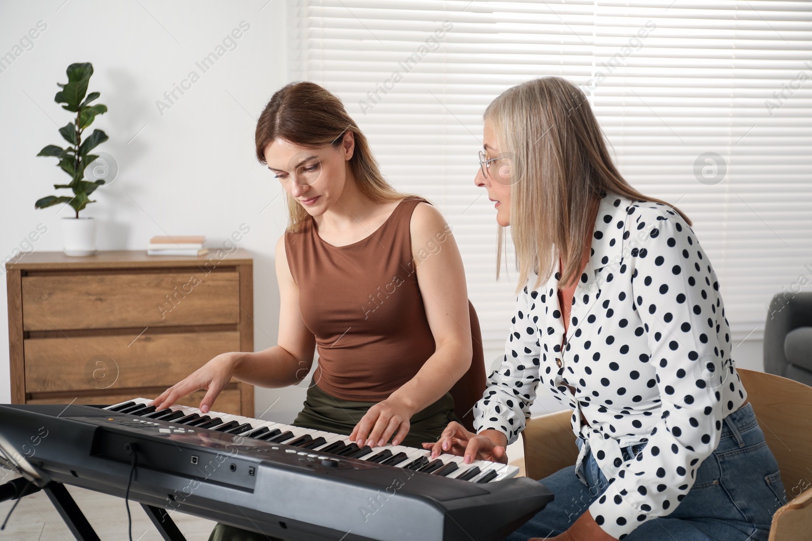 Photo of Tutor teaching woman to play piano indoors