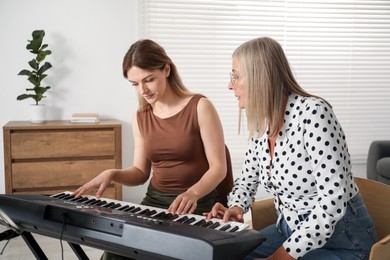 Photo of Tutor teaching woman to play piano indoors