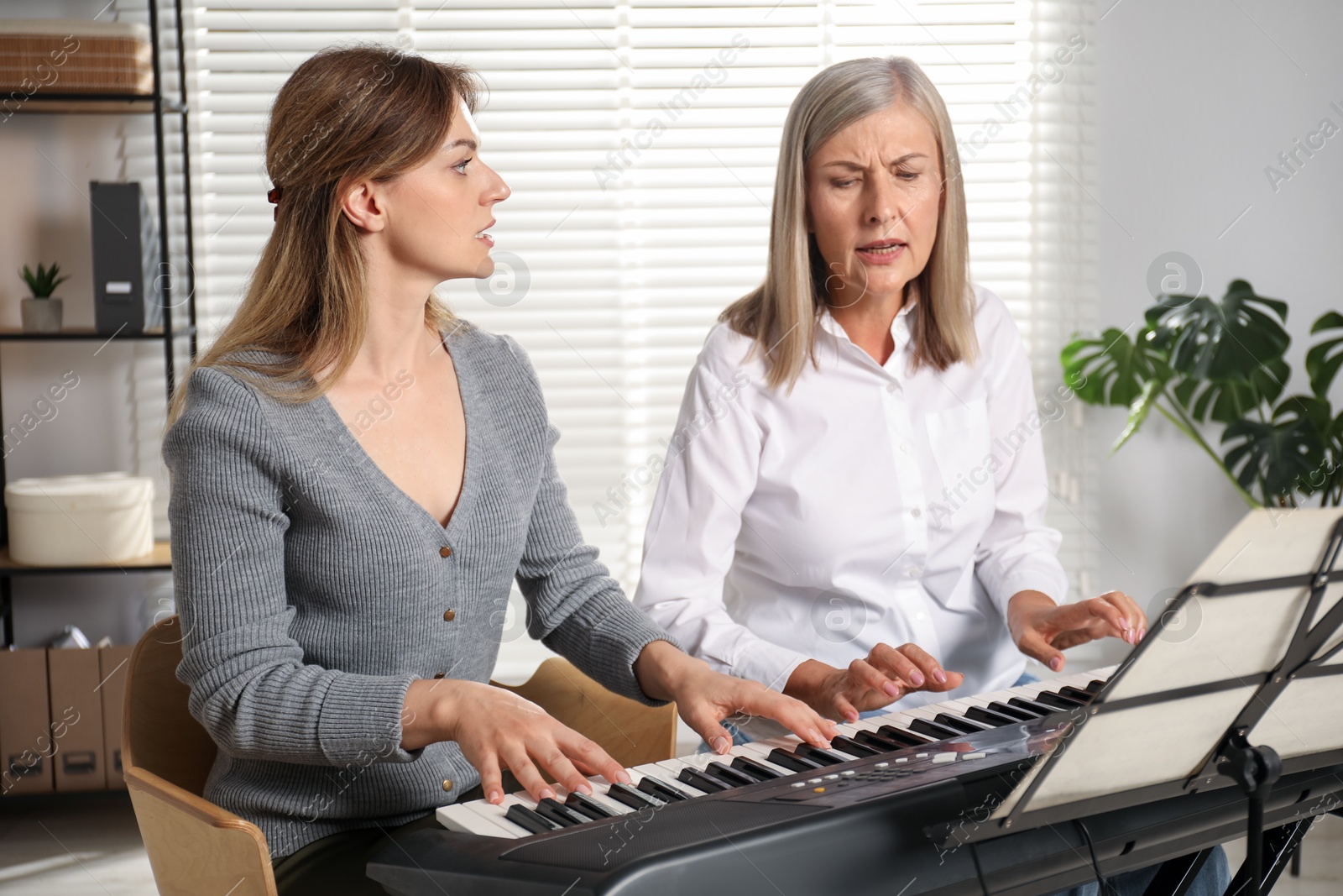 Photo of Tutor teaching woman to play piano indoors
