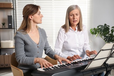 Photo of Tutor teaching woman to play piano indoors