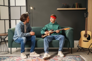 Photo of Tutor teaching man to play guitar on sofa indoors