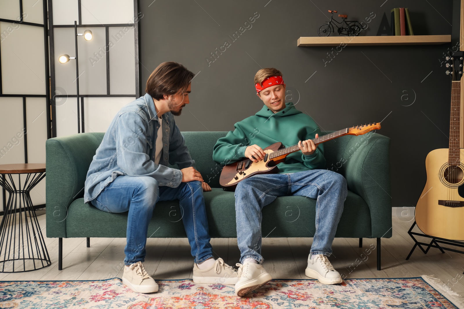 Photo of Tutor teaching man to play guitar on sofa indoors