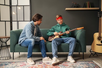 Photo of Tutor teaching man to play guitar on sofa indoors
