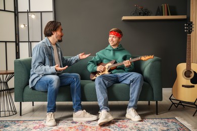 Photo of Tutor teaching man to play guitar on sofa indoors
