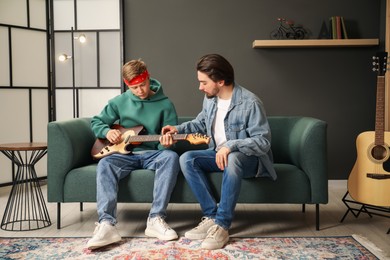 Photo of Tutor teaching man to play guitar on sofa indoors